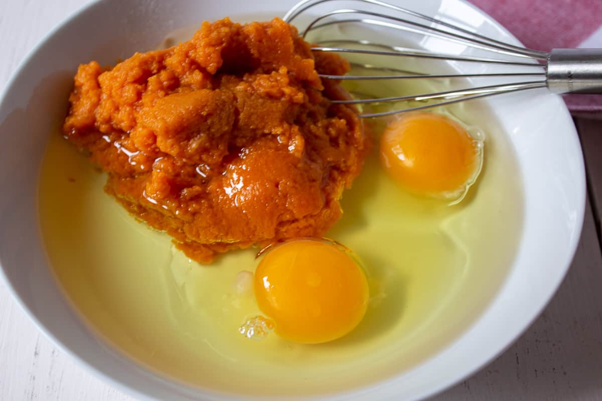 Eggs and pumpkin puree in a bowl with a wire whisk.