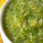 Corn chips sprinkled around a bowl of green salsa.