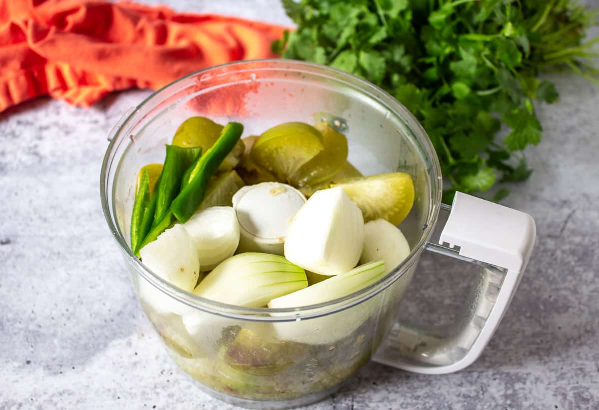 Onions, peppers and tomatillos in a food processor bowl.