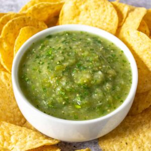 A white bowl filled with green salsa verde surrounded by tortilla chips.