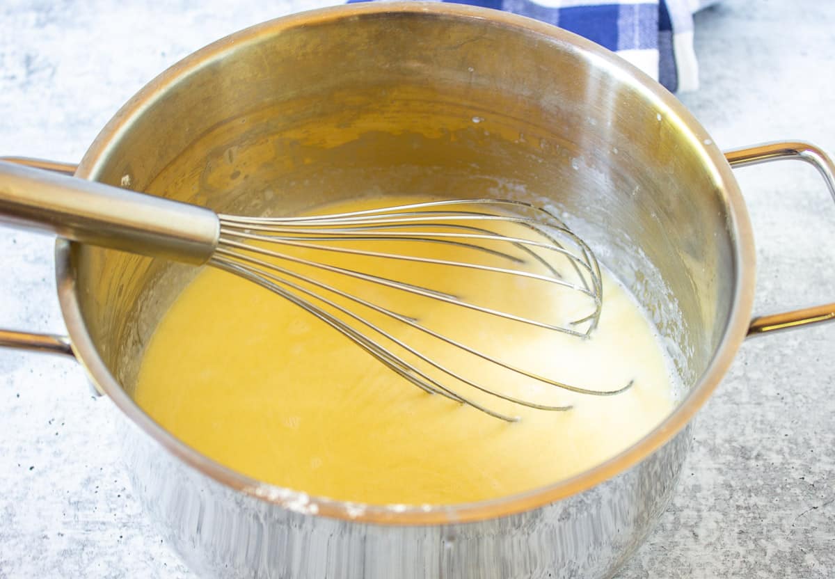 A thick sauce in a sauce pan with a whisk.