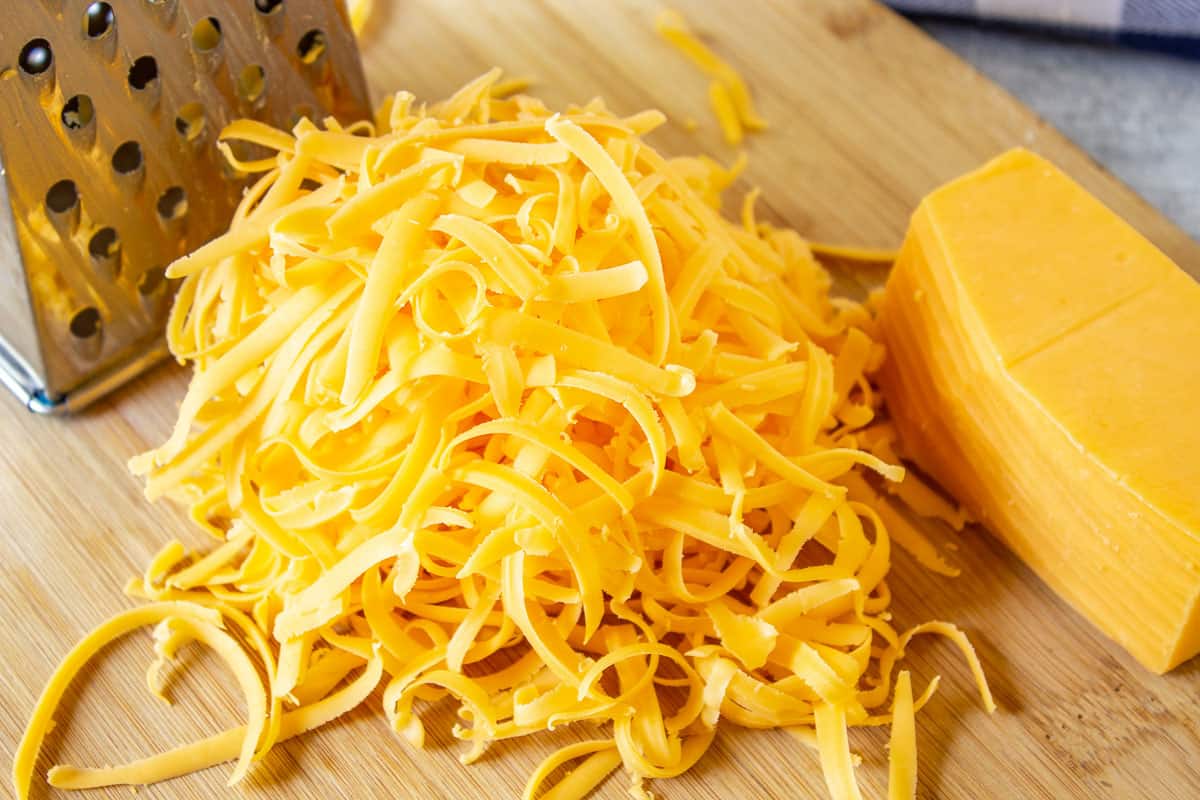 A pile of shredded cheddar cheese on a wooden board.