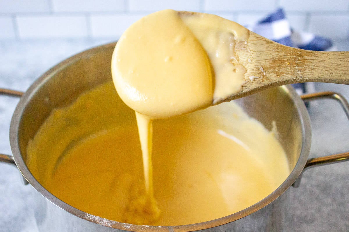 A creamy cheese sauce dripping off a wooden spoon.