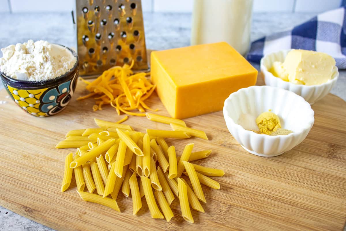 Pasta, cheese, butter, milk and seasonings displayed on a wooden board.