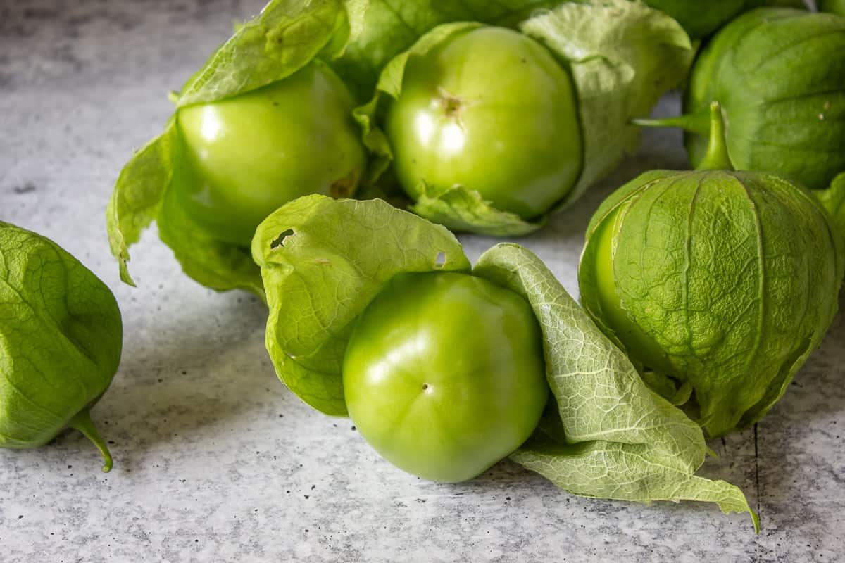 Green tomatillos with husks on a board.