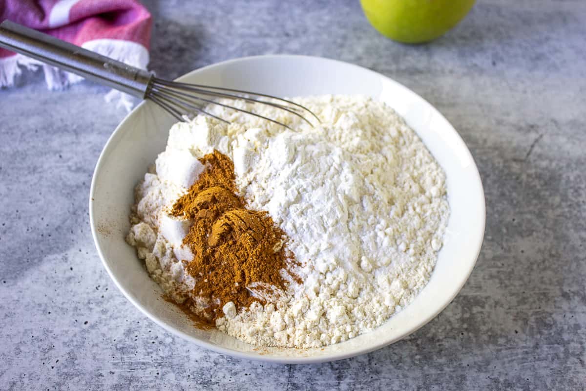 Flour and cinnamon in a white bowl with a small wire whisk.