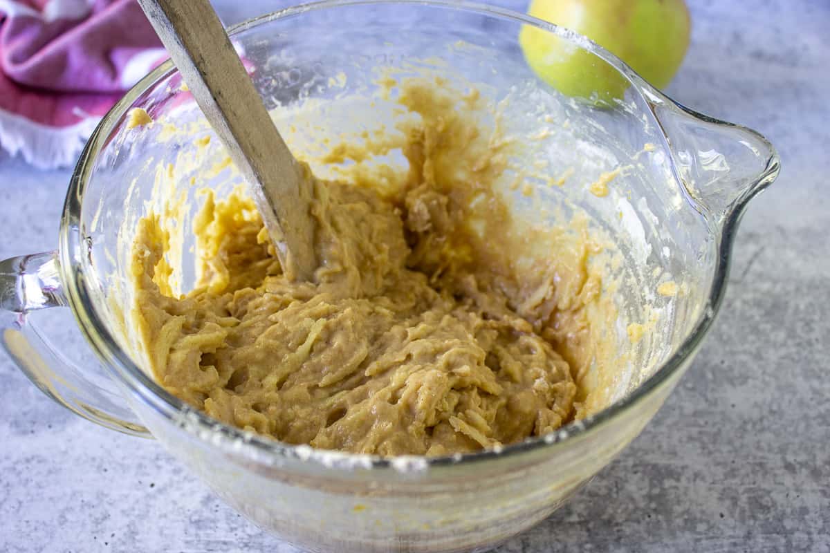 Apple bread batter in a glass bowl with a wooden spoon.