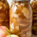 Canning jars filled with apple pie filling with fresh apples in front of the jars.