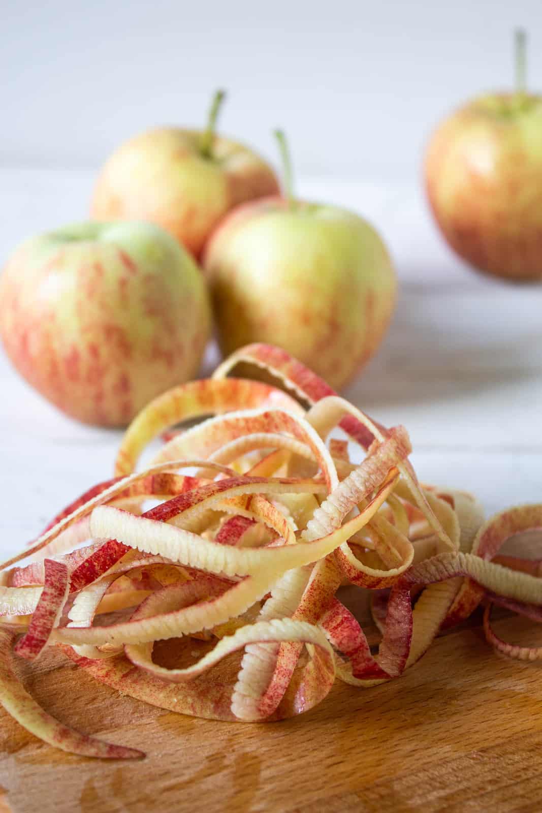 Ribbons of apple peel piled on a cutting board with more apples behind the peels.