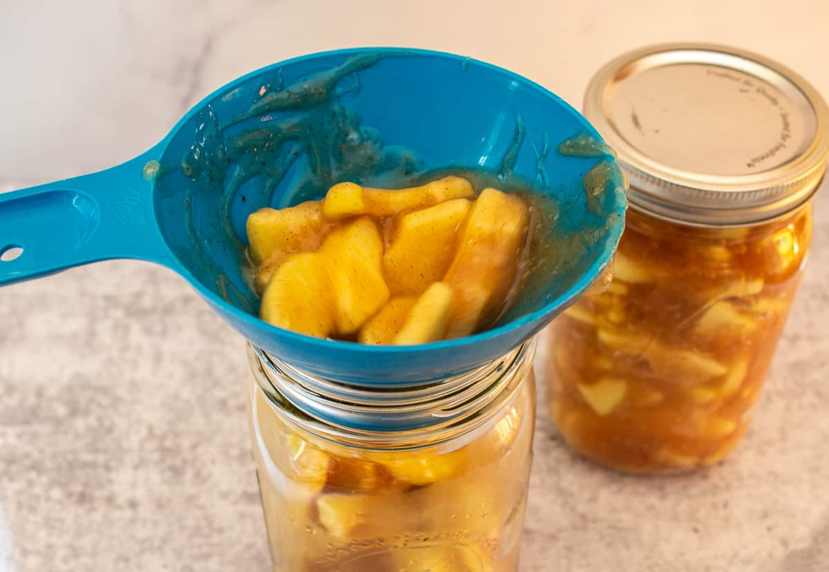 A blue funnel over a glass canning jar filled with apples.