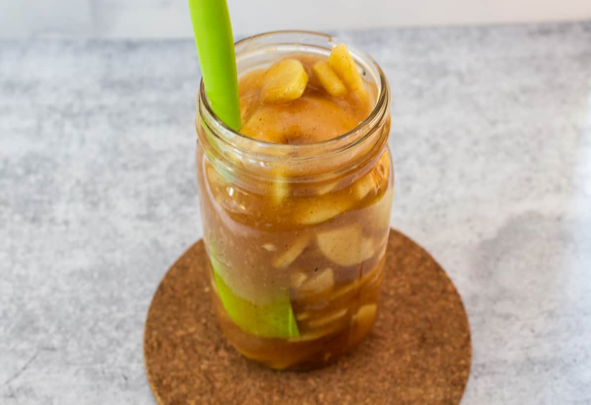 A green spatula in a glass jar filled with apple pie filling.