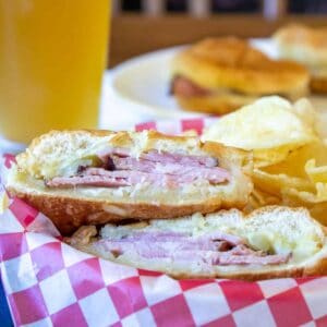 A ham sandwich cut in half in a basket with red and white paper.