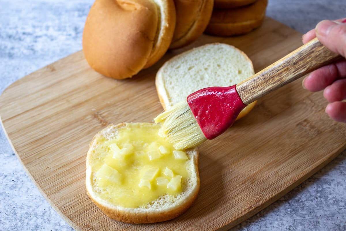 Butter and onions spread on the bottom of a hamburger bun with a pastry brush.