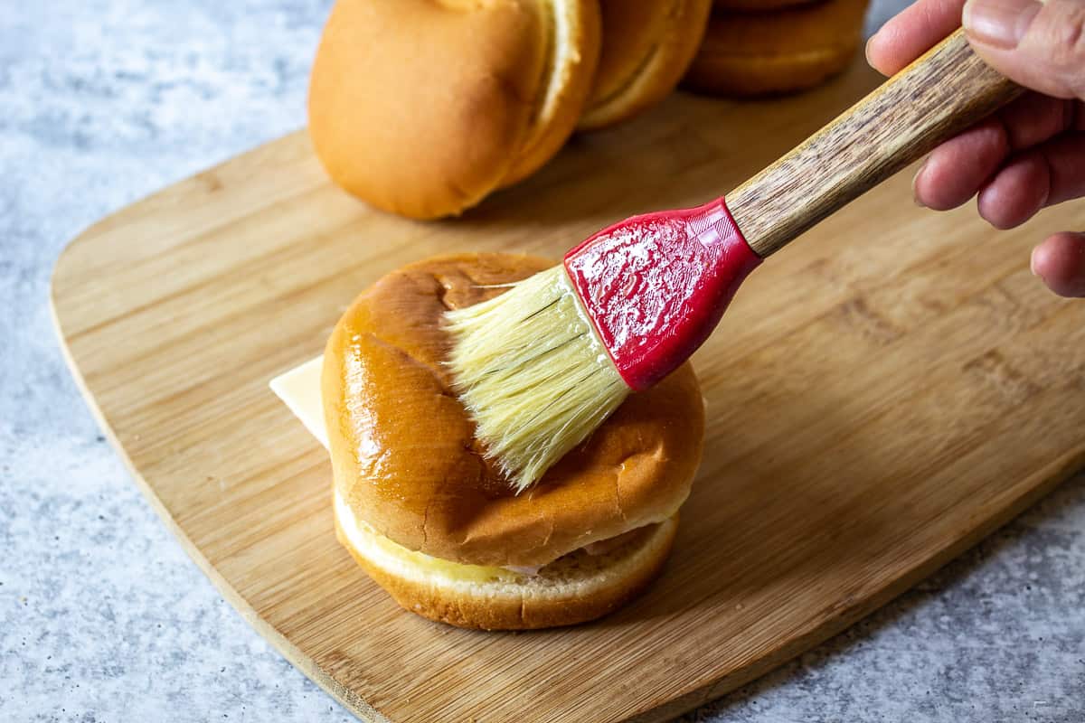 The top of a hamburger bun being brushed with melted butter.