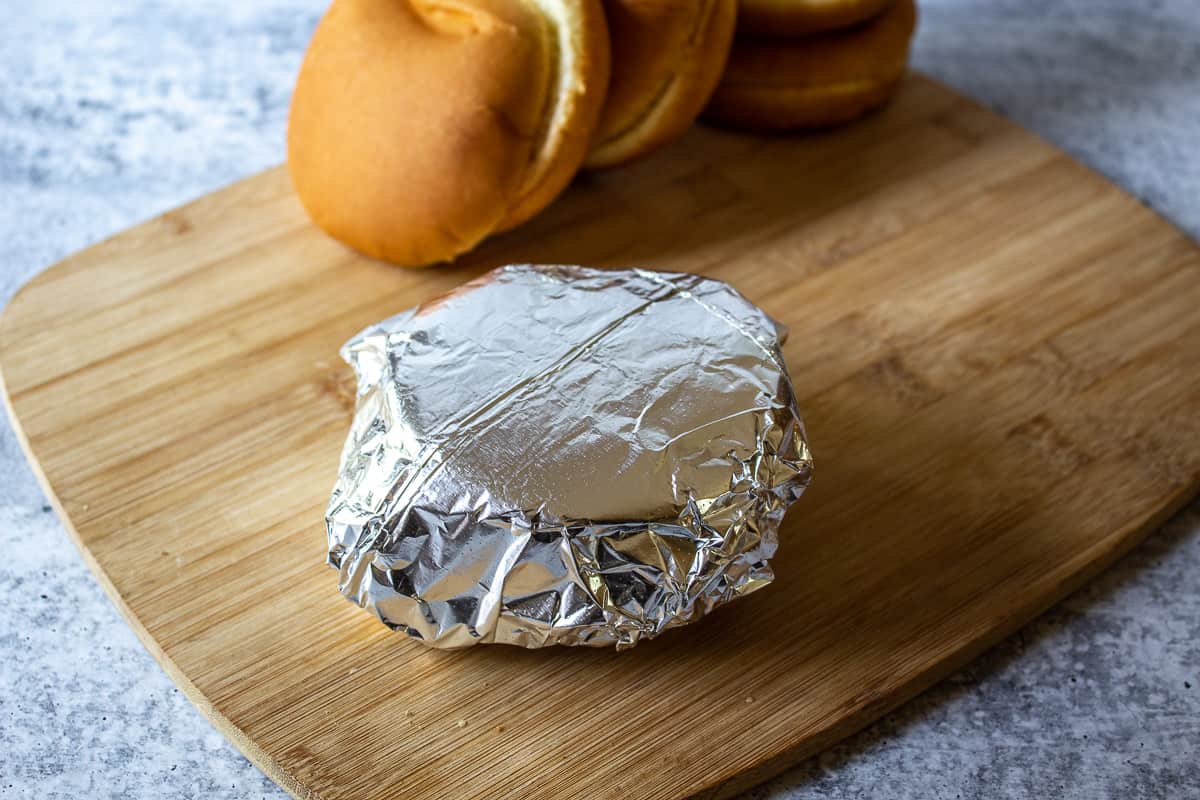 A sandwich wrapped in foil on a wooden board.