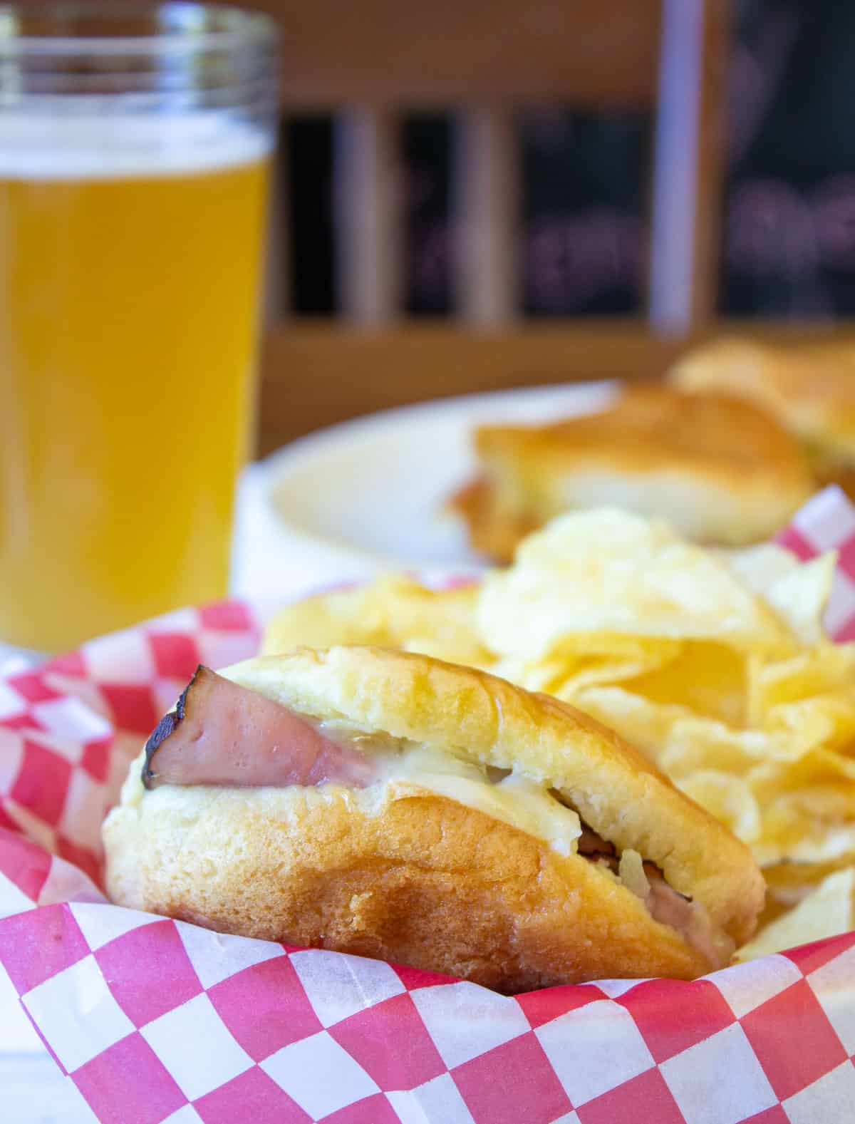 A hamburger bun filled with ham in a basket with potato chips.