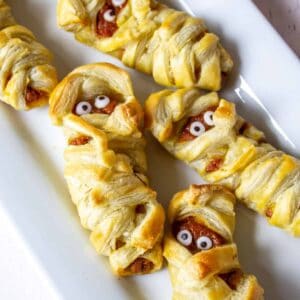 Mummy hand pies with candy eyes arranged on a white platter.