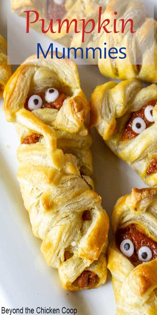 A white plate filled with small mummies with a pumpkin filling and candy eyes.