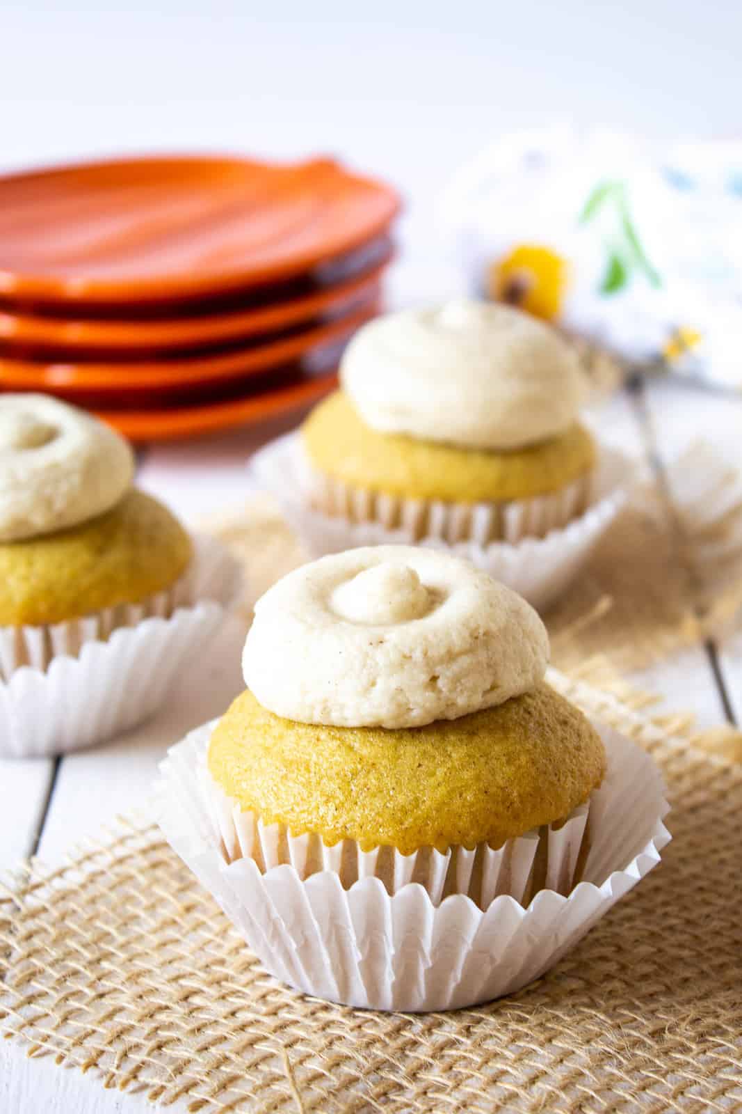 A cupcake with a dollop of frosting on a board with a piece of burlap.