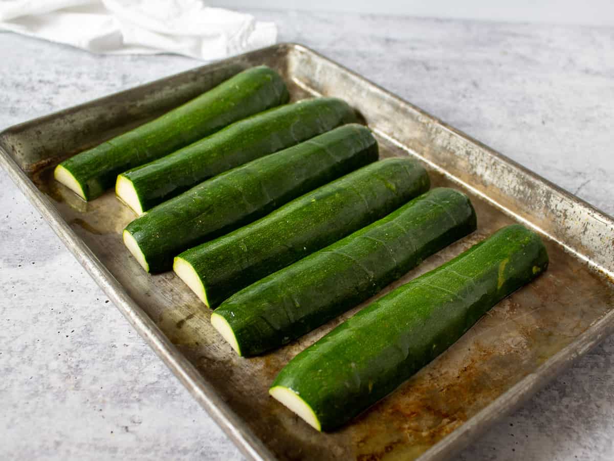 Zucchinis faced down on a baking sheet drizzled with olive oil. 