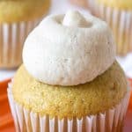 A cupcake with frosting on an orange plate.