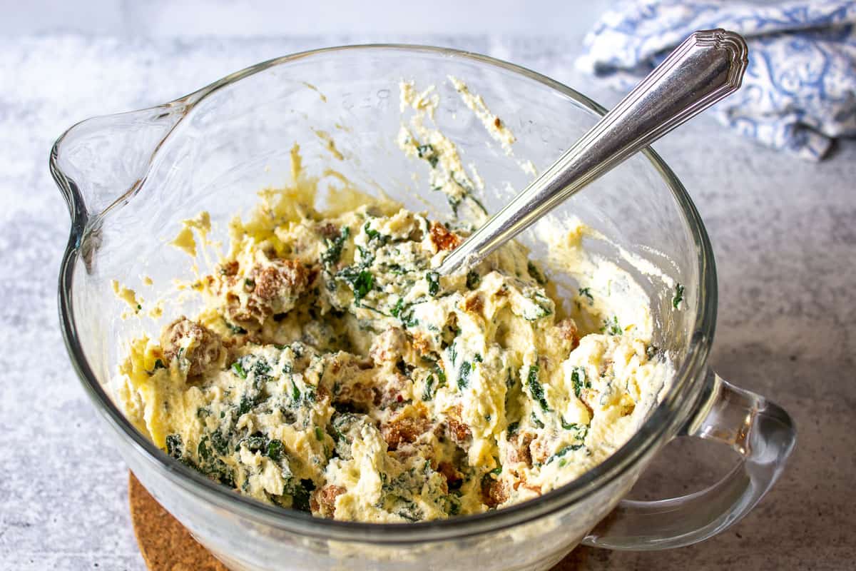 Cheese mixture in a glass bowl with a metal spoon.