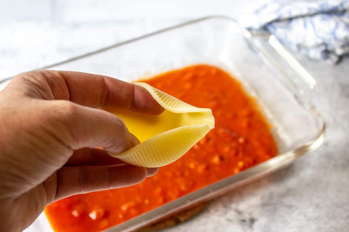 A pasta shell being held open with one hand.