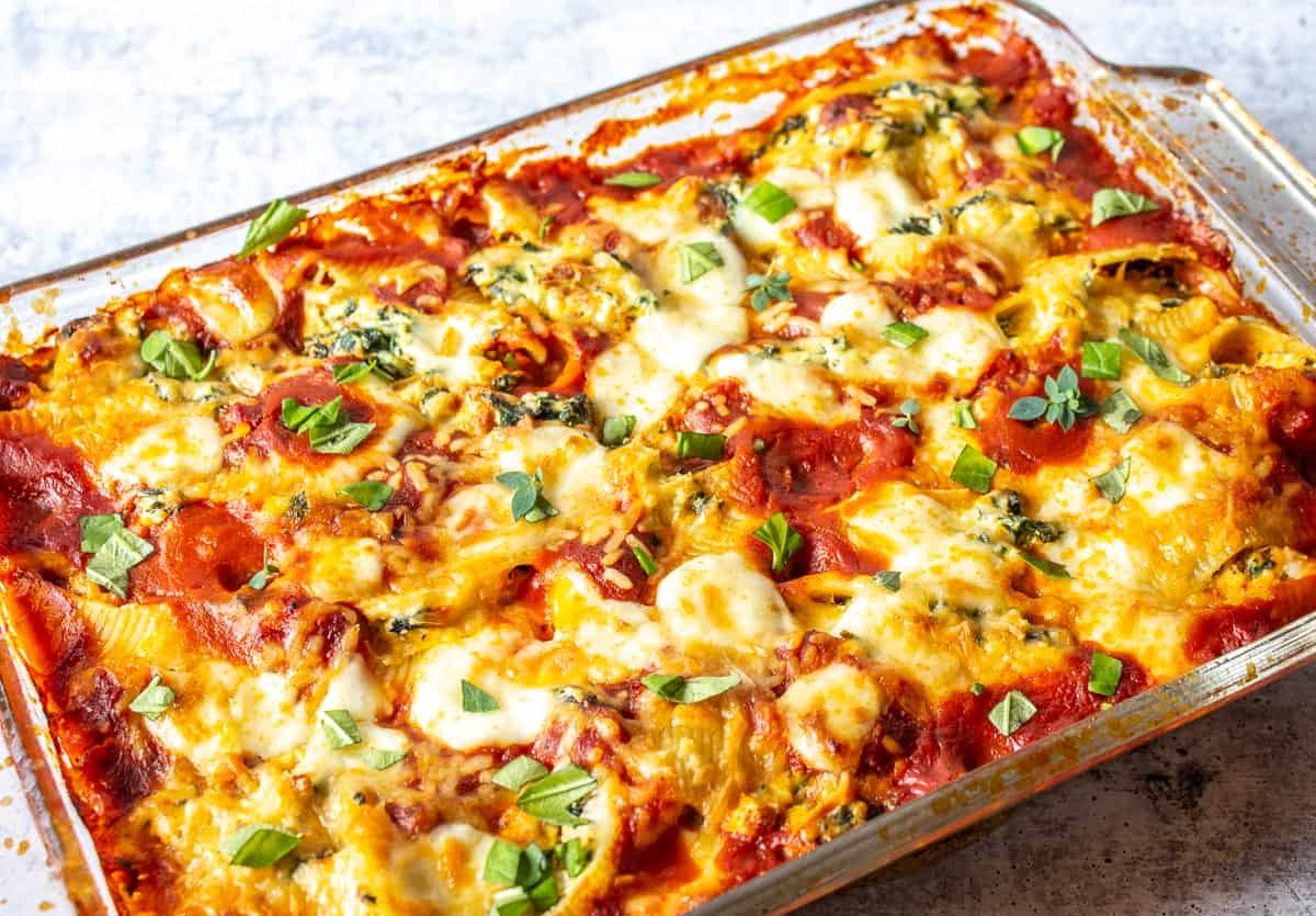 A casserole dish filled with stuffed pasta and topped with fresh herbs.