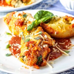 Three stuffed pasta shells with tomato sauce, parmesan cheese and fresh basil on top.