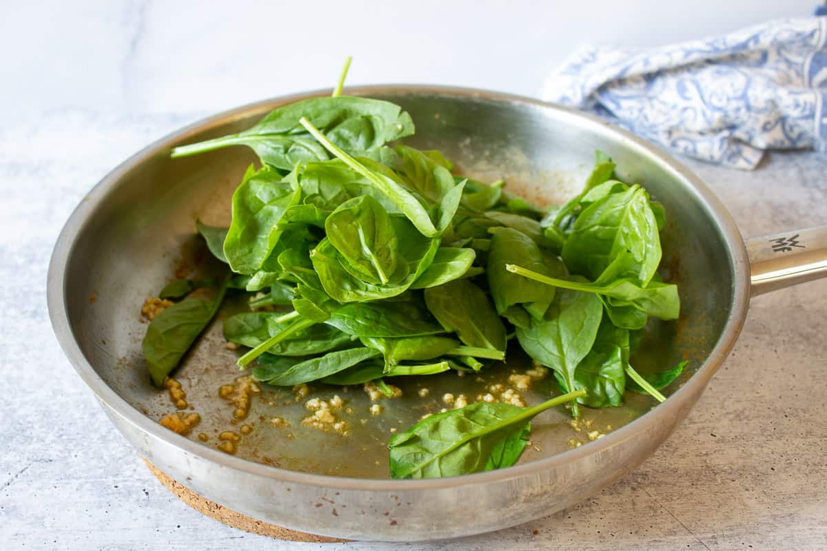 Fresh spinach in a pan with cooked garlic.