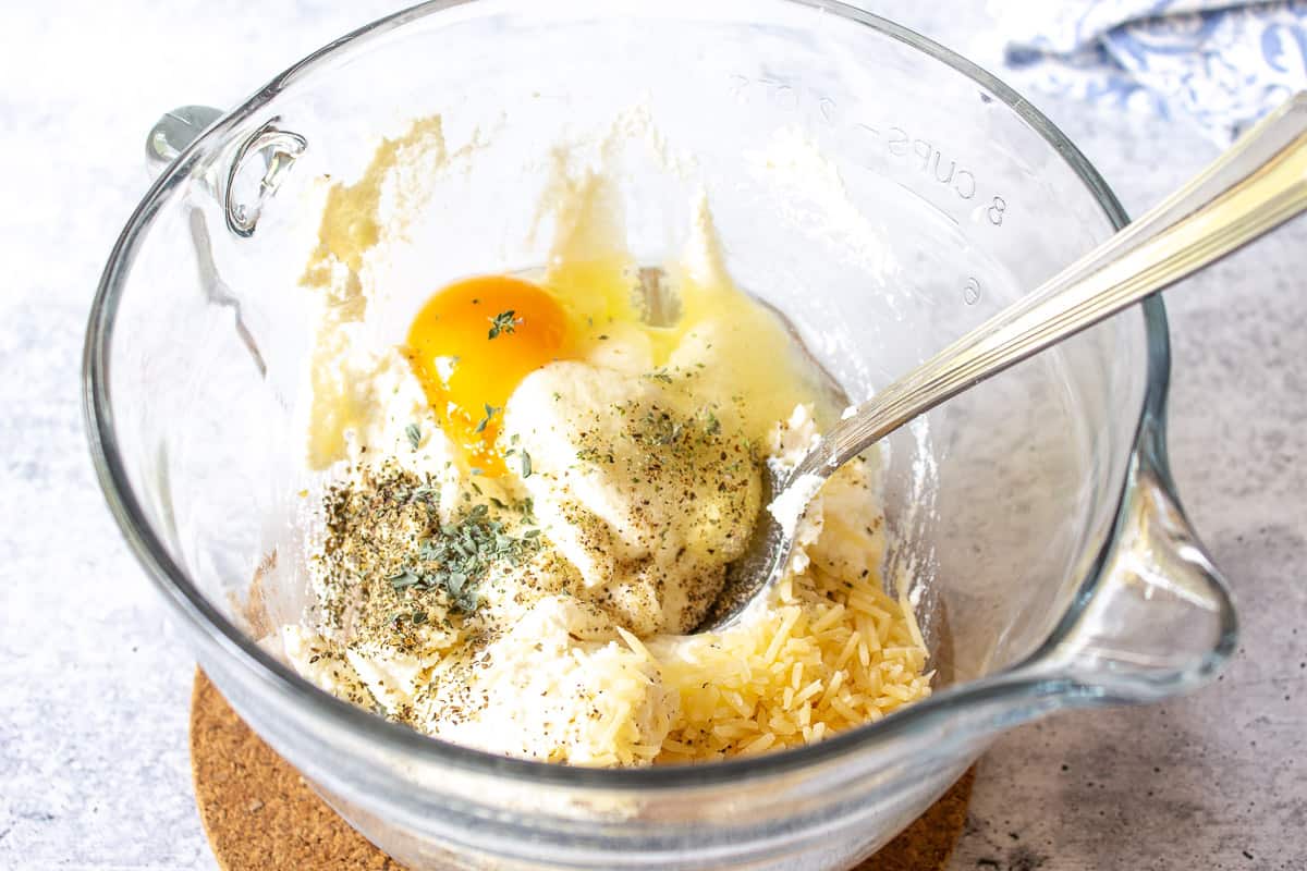 A glass bowl with ricotta, parmesan, an egg and seaonings.