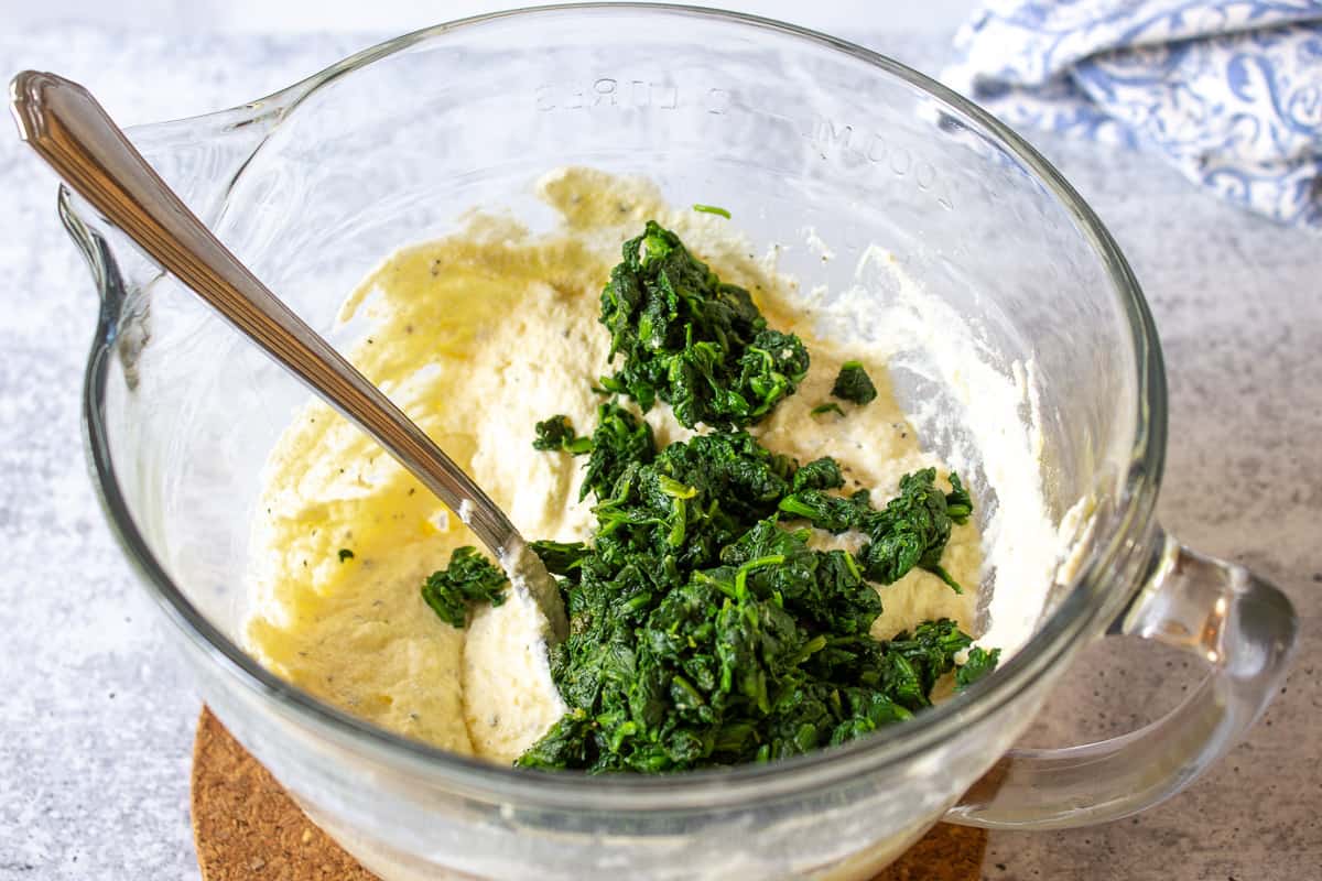 Chopped spinach on top of a cheese mixture in a glass bowl.