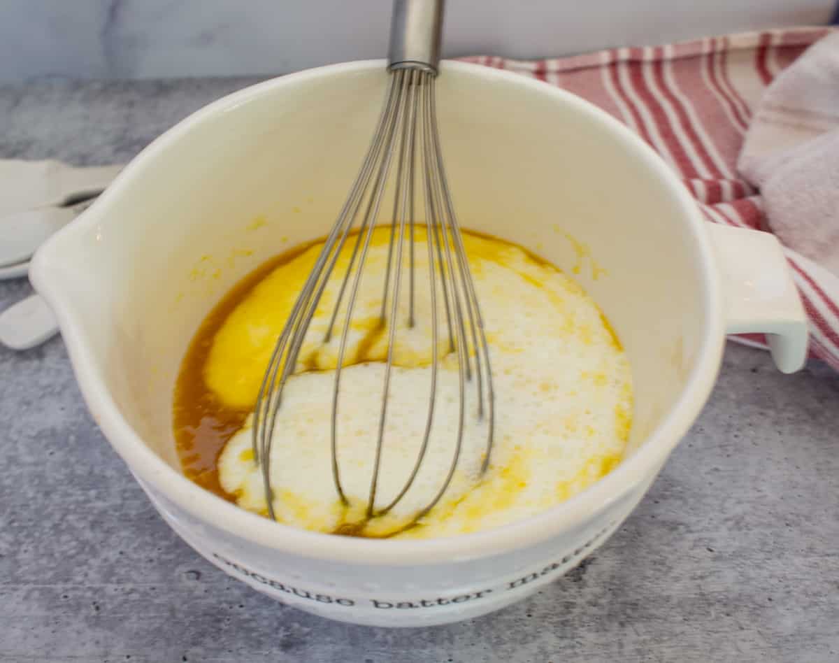 A white mixing bowl and a whisk with eggs and milk.