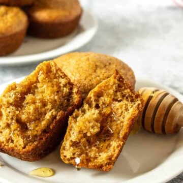 Bran muffin split in half and drizzled with honey on a white plate.