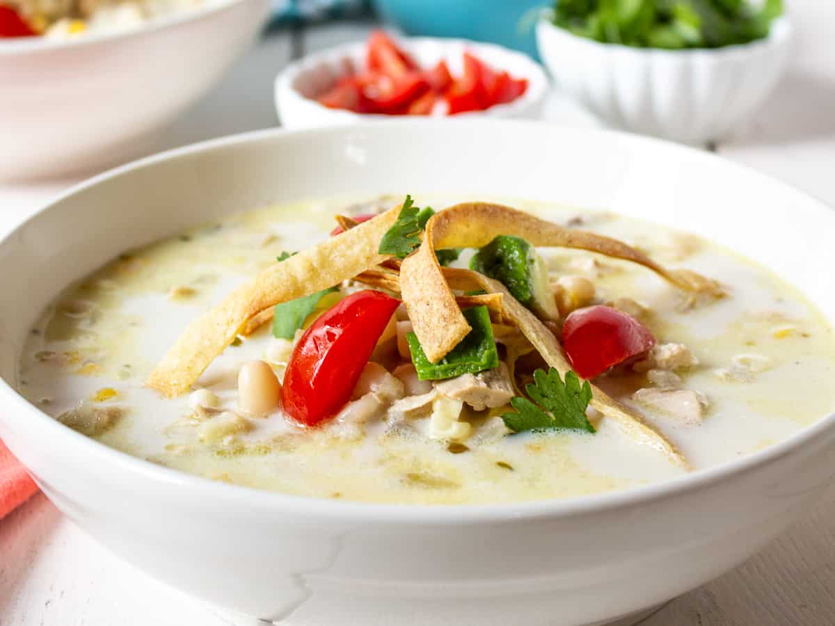 White chicken chili in a large bowl topped with fresh tomatoes, cilantro and tortilla strips.