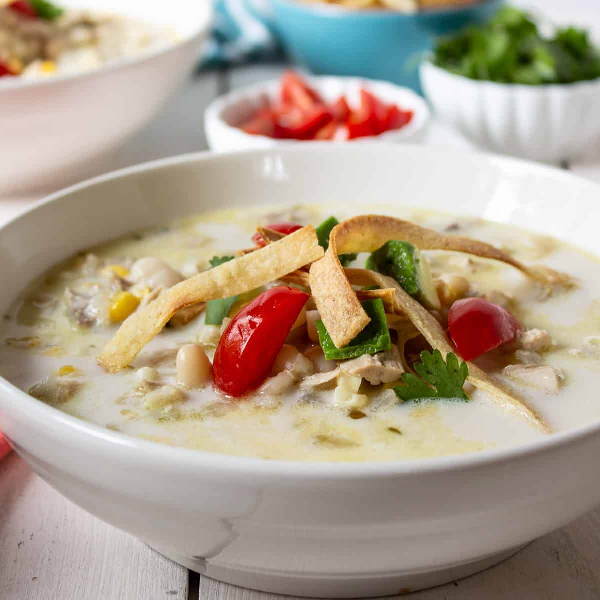 A bowl of white chicken chili topped with fresh tomatoes and tortilla strips.