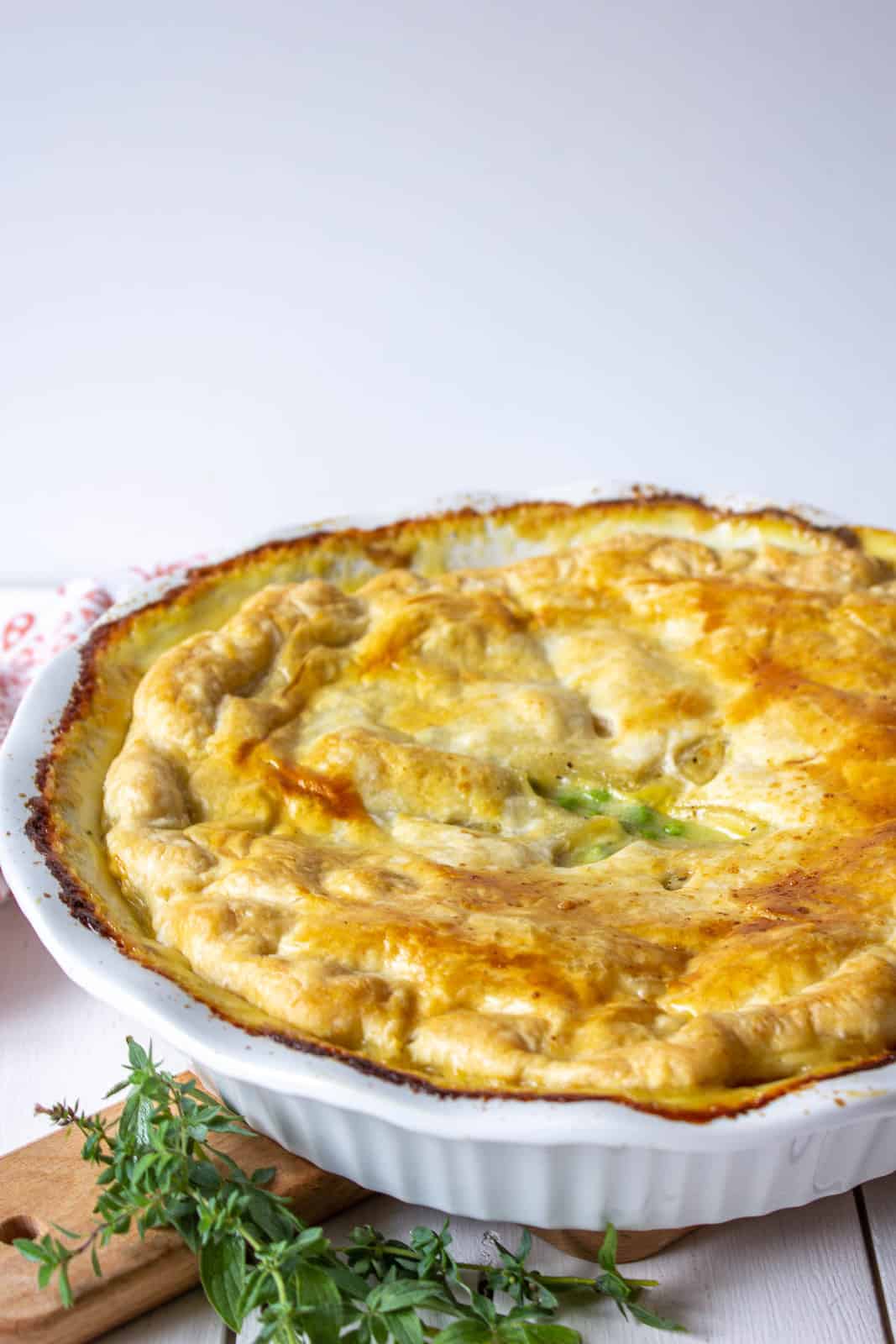 A white pie dish filled with a savory filling and topped with a puff pastry crust.