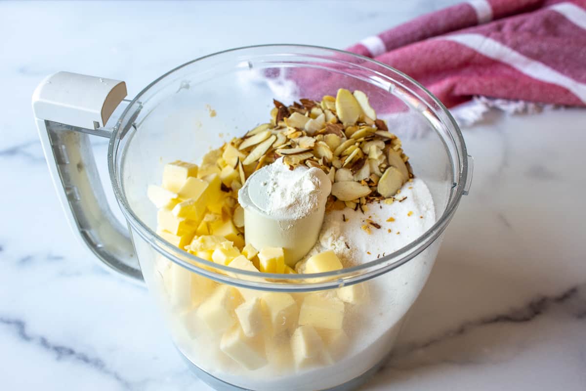 A food processor bowl filled with flour, butter and almonds.