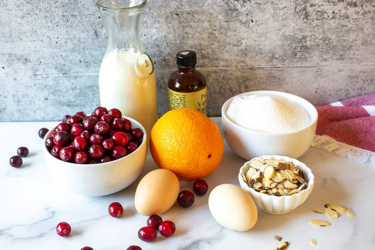 A display of cranberries, eggs, almonds, and an orange on a white surface.