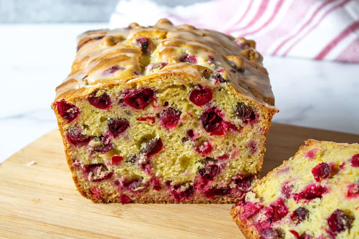 A loaf of bread filled with cranberries cut in half on a wooden cutting board.