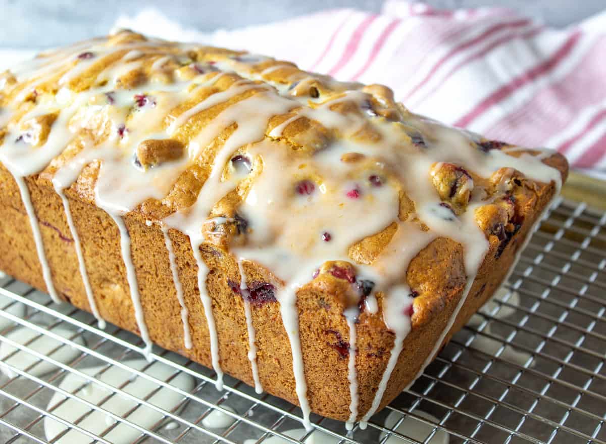 A loaf of bread with cranberries and topped with a glaze drizzled over the top.