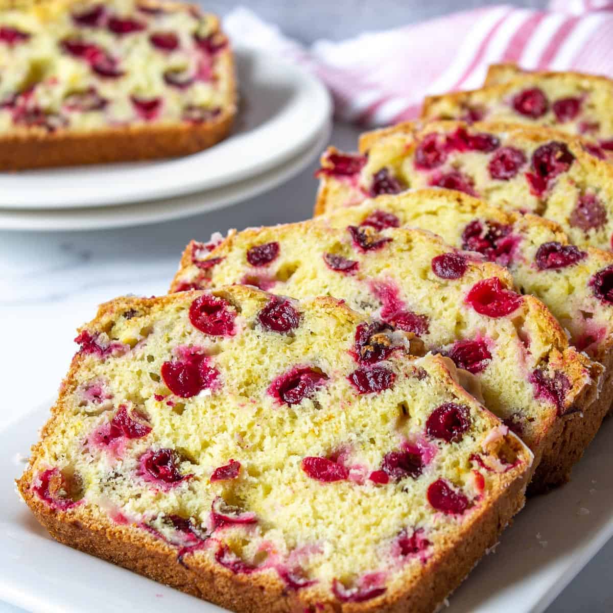 Slices of a quick bread with berries overlapping each other on a white tray.