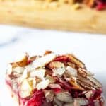 A cranberry bar topped with sliced almonds on a white piece of parchment paper.