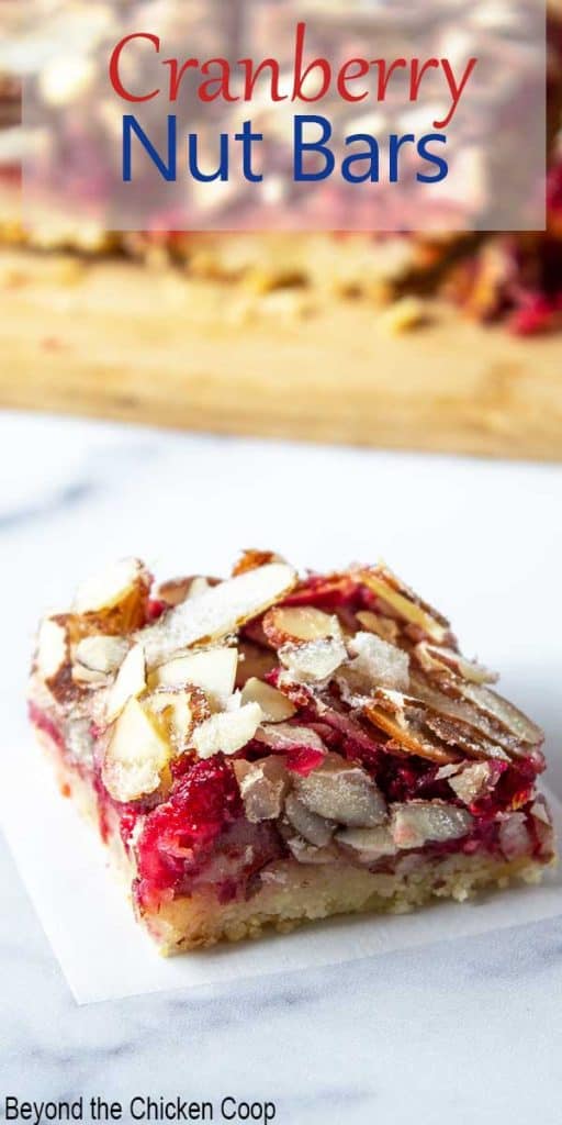 A cranberry bar topped with sliced almonds on a white piece of parchment paper.