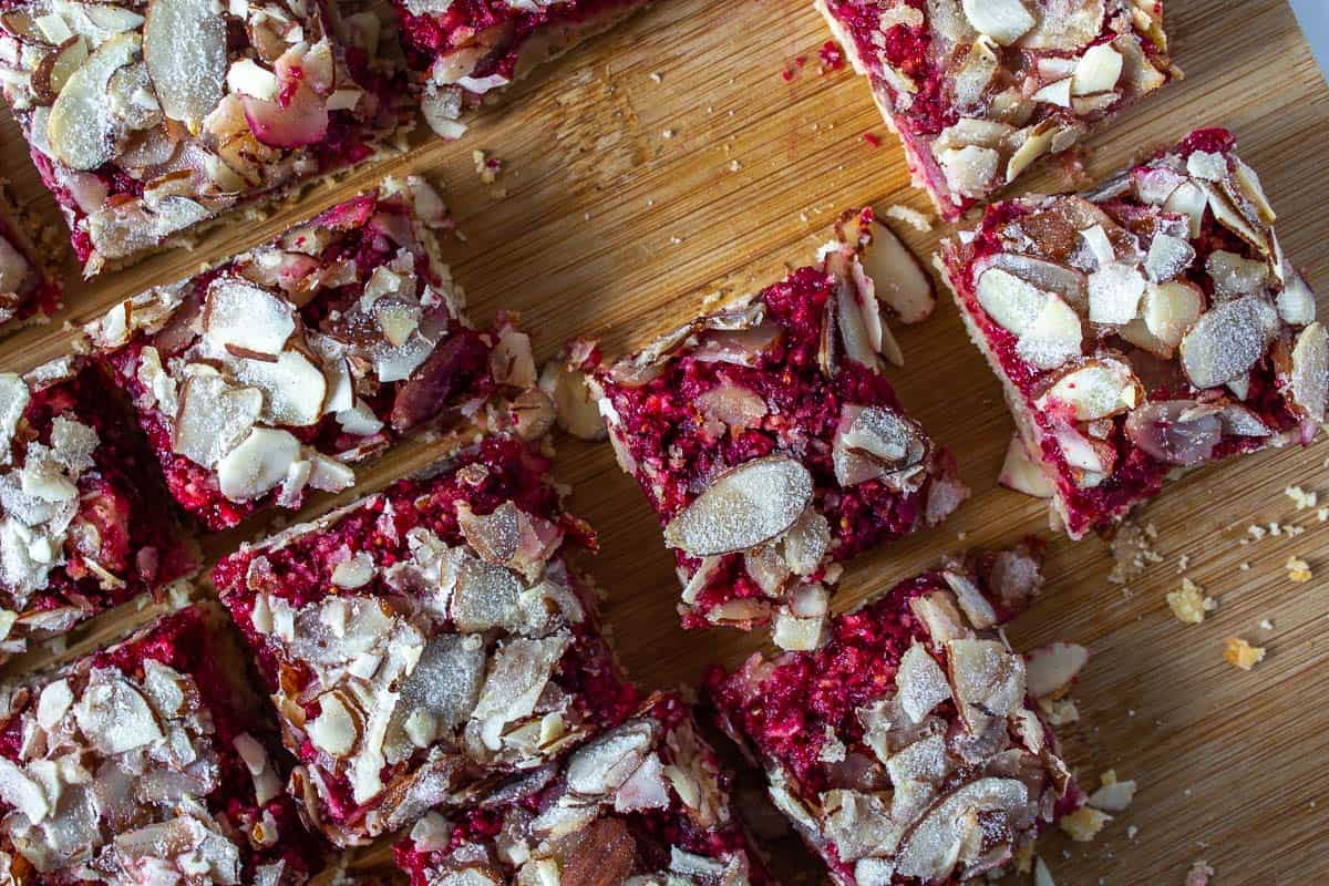 Cranberry bars topped with sliced almonds on a wooden cutting board.