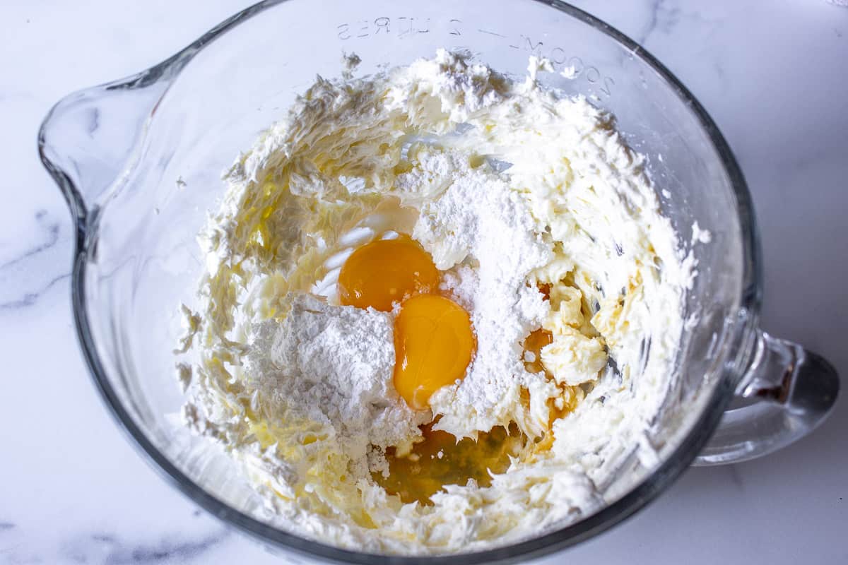 Cream cheese in a glass bowl with egg yolks, powdered sugar and vanilla.