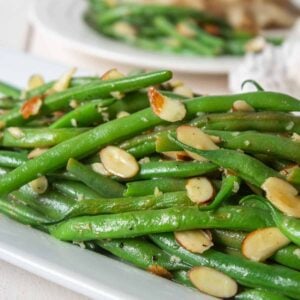 Brightly colored green beans topped with slivered almonds on a white platter.
