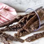 A pile of dried jerky on a white surface with a red and white towel.