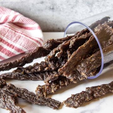 A pile of dried jerky on a white surface with a red and white towel.