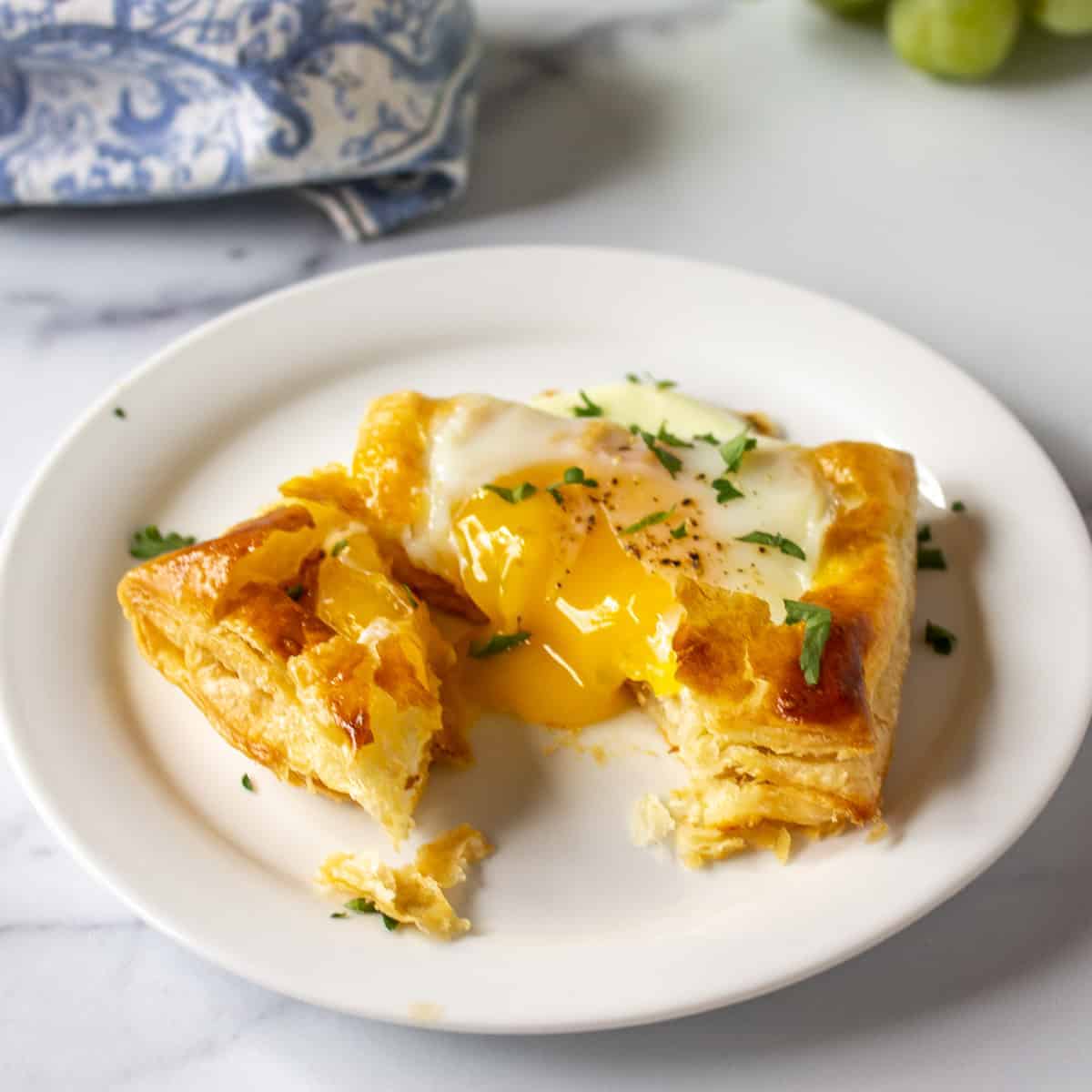 A baked egg in a puff pastry shell with the yolk running on the plate.